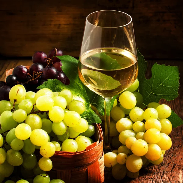 Witte wijn en groene druiven in een rieten mand in een wijnkelder — Stockfoto