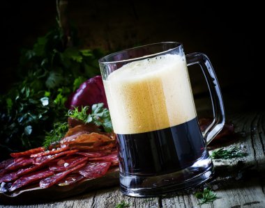 Büyük bardak koyu köpük bira, sosis ve et meze