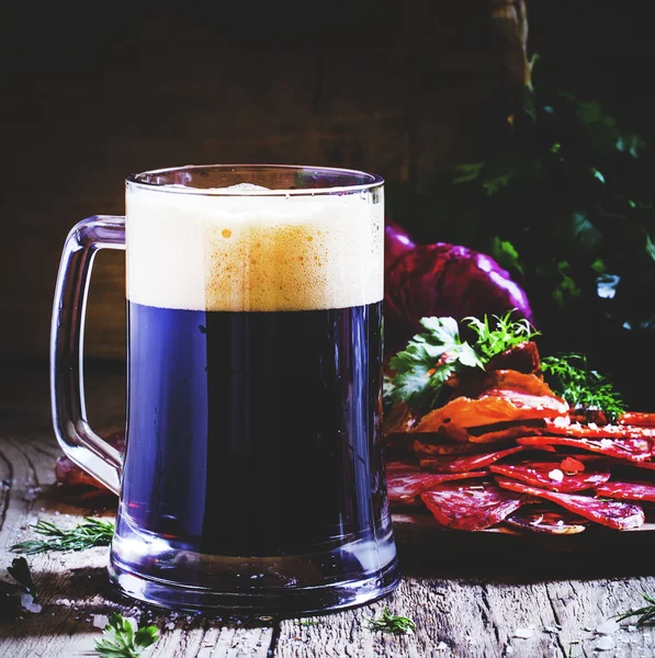 Grande bicchiere di birra scura schiuma, salsiccia e antipasti di carne — Foto Stock
