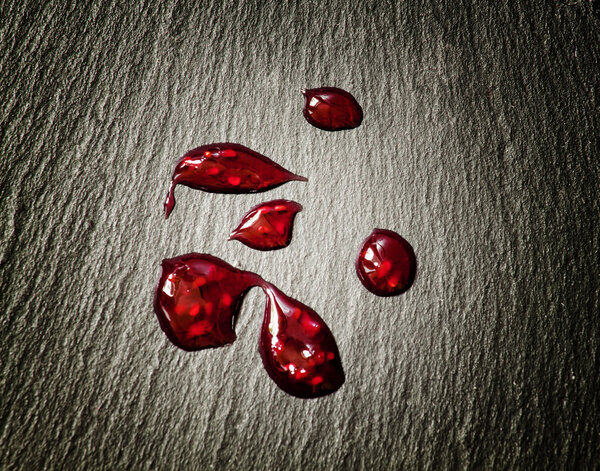 Drops of red raspberry jam on black stone background