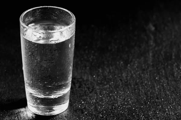Vidrio con una bebida transparente sobre fondo oscuro —  Fotos de Stock