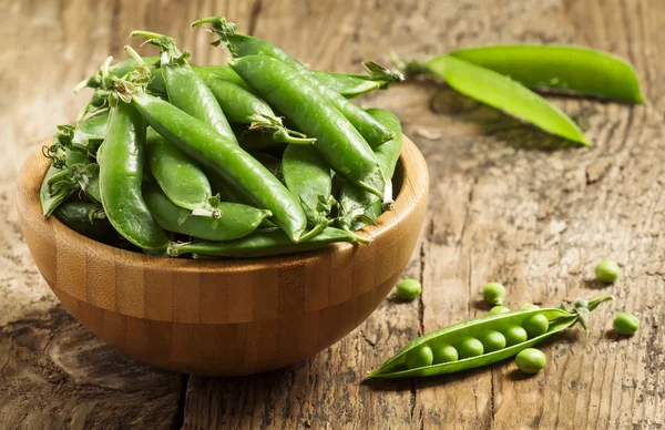 Tige de petits pois verts frais dans un bol sur une vieille table en bois — Photo