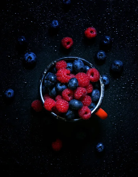 Framboesas e mirtilos em caneca de esmalte velha — Fotografia de Stock