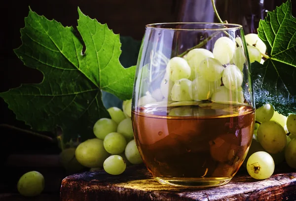 Vinho branco em um copo, uvas verdes com folhas em uma adega — Fotografia de Stock