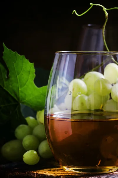 Vinho branco em um copo, uvas verdes com folhas em uma adega — Fotografia de Stock