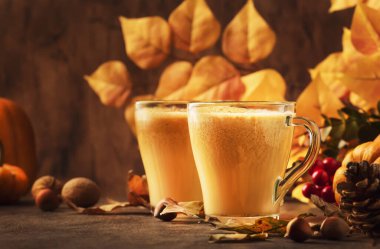 Balkabağı aromalı latte ya da eski ahşap masada cam bardakta kahve. Sonbahar ya da kış sıcak içecek ve içecekler. Düşen yapraklar, küçük balkabakları, çam kozalakları ve fındıklı sonbahar dekorları. 