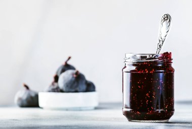 Cam kavanozda incir reçeli ve taze mavi incir. Ev yapımı hazırlıklar ve konserveler. Gri arkaplan, alanı kopyala