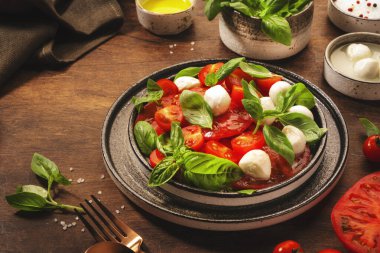 Caprese, kırmızı domatesli İtalyan salatası ve yeşil fesleğen yapraklı mozzarella peyniri. Üst manzara, ahşap masa.