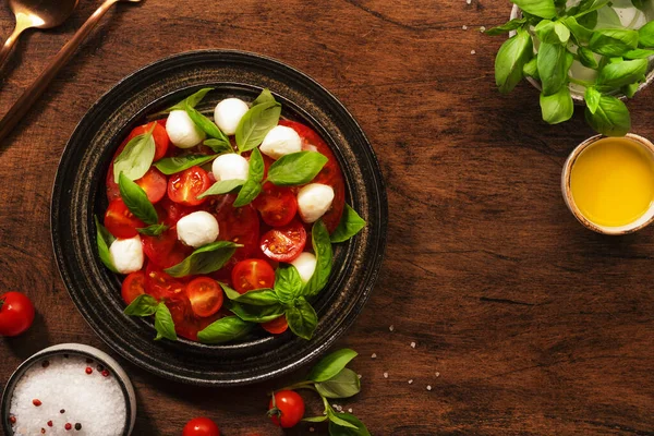 カプレーゼ イタリアのサラダにトマトとモッツァレラチーズと緑のバジルの葉 トップビュー 木製のテーブル — ストック写真