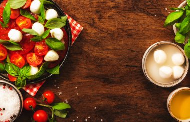 Caprese, kırmızı domatesli İtalyan salatası ve yeşil fesleğen yapraklı mozzarella peyniri. Üst manzara, ahşap masa.