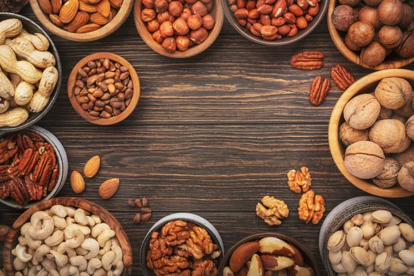 Assortment of nuts in bowls. Cashews, hazelnuts, walnuts, pistachios, pecans, pine nuts, peanuts, macadamia, almonds, brazil nuts. Food mix on wooden background, top view, copy space