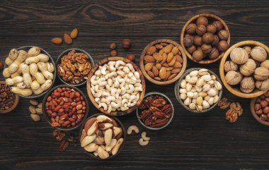 Fındık çeşitleri kaselerde. Fındık, fındık, fındık, fıstık, fıstık, çam fıstığı, yer fıstığı, macadamia, badem, Brezilya fındığı. Ahşap arkaplanda yiyecek karışımı, üst görünüm, kopyalama alanı