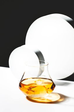 Viski, viski veya viskiyle çağdaş bir hayat. Siyah beyaz arka planda siyah buzlu, geometrik küplü ve daireli bir bardak viski.