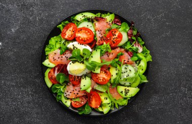 Keto diyet salatası, tuzlu somon, avokado, yumurta, susam tohumu, zeytin yağı, domates ve karışık otlar. Siyah arkaplan, üst görünüm, kopyalama alanı