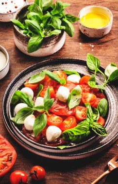 Kırmızı domatesli İtalyan salatası Caprese ve yeşil fesleğen yapraklı mozzarella peyniri ve zeytinyağı sosu. Üst manzara, ahşap masa.