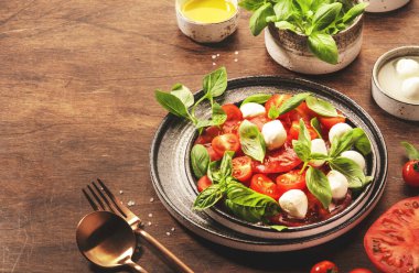 Kırmızı domatesli İtalyan salatası Caprese ve yeşil fesleğen yapraklı mozzarella peyniri ve zeytinyağı sosu. Üst manzara, ahşap masa.