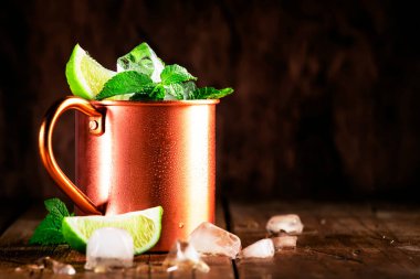 Moskova katırı veya nane likörü, limonlu, zencefilli bira, votka ve naneli bakır bardakta alkollü kokteyl. Tahta masa, bakır bar aletleri.
