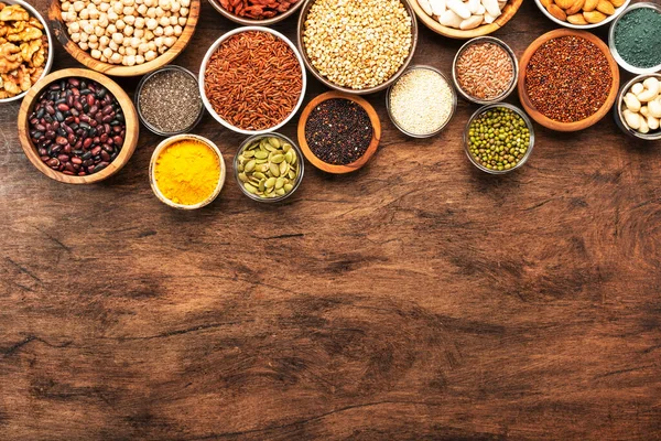 stock image Superfoods, legumes, cereals, nuts, seeds set in bowls on wooden background. Superfood as chia, spirulina, beans, goji berries, quinoa, turmeric and other. Top view