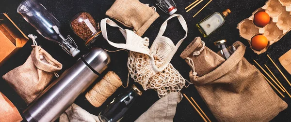 Geri dönüşümlü, yeniden kullanılabilir çevre dostu çantalar, paket, şişe, kutu ve konteynırlar, ağ torbası. Gri masa, üst manzara. Sıfır atık, plastiksiz ve sürdürülebilir yaşam konsepti