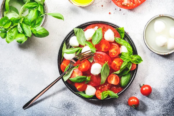 Kırmızı domatesli Caprese salatası ve taze yeşil fesleğen yapraklı beyaz mozzarella peyniri. Gri masa. Üst görünüm