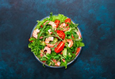 Domatesli karides salatası, marul, roka, avokado, salatalık ve limon sosu mavi masada. Sağlıklı beslenme, temiz yemek konsepti. Üst görünüm 