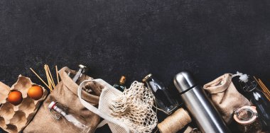 Geri dönüşümlü, yeniden kullanılabilir çevre dostu çantalar, paket, şişe, kutu ve konteynırlar, ağ torbası. Gri masa, üst manzara. Sıfır atık, plastiksiz ve sürdürülebilir yaşam konsepti