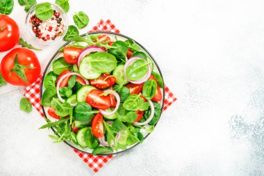 Ispanaklı, domatesli, roka, salatalık ve kırmızı soğanlı vegan salatası. Taze ve sağlıklı yiyecekler. Gri taş masa. Üst görünüm