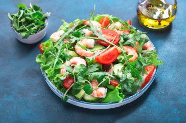 Domatesli karides salatası, marul, roka, avokado, salatalık ve limon sosu mavi masada. Sağlıklı beslenme, temiz yemek konsepti. Üst görünüm 