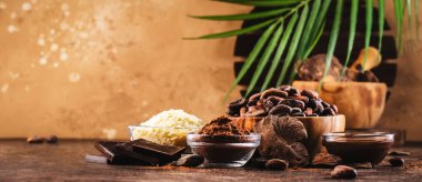 Çeşitli kakao ürünleri seti: fasulye, toz, tereyağı, koyu çikolata, ahşap masa arkasındaki rendelenmiş kakao.