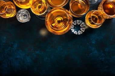 Sert alkollü içecekler, bardaklarda içki ve damıtma: votka, konyak, tekila, viski. Mavi arkaplan, üst görünüm, sert ışık