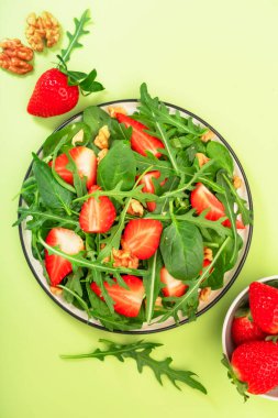 Ispanak, roka, ceviz, balzamik sirke ve yeşil arka planda zeytinyağı soslu çilekli vejetaryen salatası. Sağlıklı yiyecekler. Üst görünüm