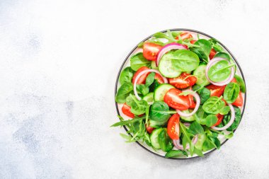 Ispanaklı, domatesli, roka, salatalık ve kırmızı soğanlı vegan salatası. Taze ve sağlıklı yiyecekler. Gri taş masa. Üst görünüm