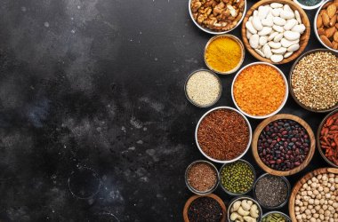 Süper yiyecekler, baklagiller, tahıllar, fındıklar, siyah arka plandaki kaselerdeki tohumlar. Chia, spirulina, fasulye, goji üzümü, kinoa, zerdeçal gibi süper yiyecekler. Boşluğu kopyala, üst görünüm