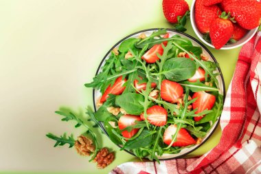 Ispanak, roka, ceviz, balzamik sirke ve yeşil arka planda zeytinyağı soslu çilekli vejetaryen salatası. Sağlıklı yiyecekler. Üst görünüm