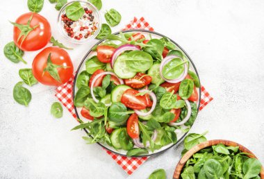 Ispanaklı, domatesli, roka, salatalık ve kırmızı soğanlı vegan salatası. Taze ve sağlıklı yiyecekler. Gri taş masa. Üst görünüm