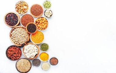 Süper yiyecekler, baklagiller, tahıllar, fındıklar, beyaz arka plandaki kaselerdeki tohumlar. Chia, spirulina, fasulye, goji üzümü, kinoa, zerdeçal gibi süper yiyecekler. Boşluğu kopyala, üst görünüm
