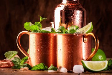 Moskova katırı veya nane likörü, limonlu, zencefilli bira, votka ve naneli bakır bardakta alkollü kokteyl. Tahta masa, bakır bar aletleri.