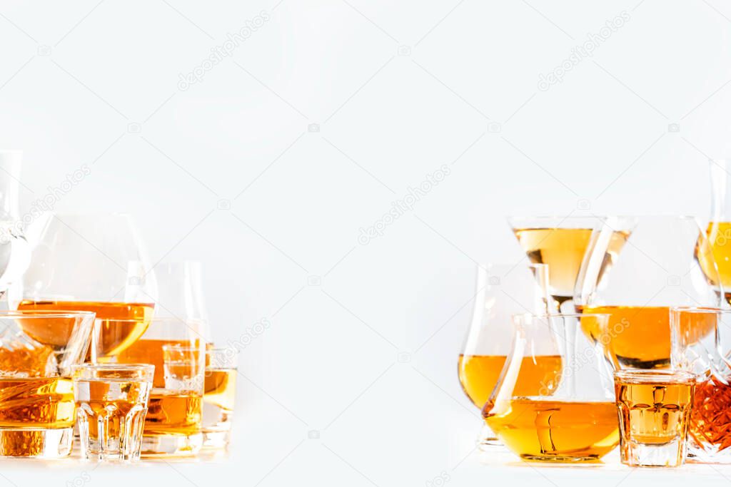 Hard strong alcoholic drinks, spirits and distillates in glasses in assortment: vodka, cognac, scotch, whiskey etc. White background, hard light