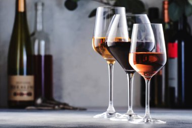 Şarap çeşitleri. Kırmızı, beyaz, şarap kadehlerinde gül şarabı ve gri arka planda şişeler. Şarap barı, dükkan, tatma konsepti.