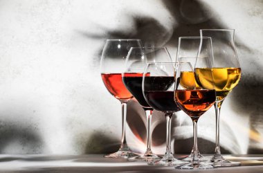 Wines assortment. Red, white, rose wine in wineglasses on gray background. Wine tasting concept. Hard sunlight and shadows from foliage clipart