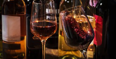 Şarap tatma. Kırmızı şarap arka planda sallanıyor. Kırmızı, beyaz ve kırmızı şarap kadehleri ve şişeler.