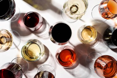 Beyaz arka planda kırmızı, gül ve beyaz şarap bardakları, üst manzara. Şarap barı, dükkan, şaraphane, şarap tatma konsepti. Sert ışık ve sert gölgeler