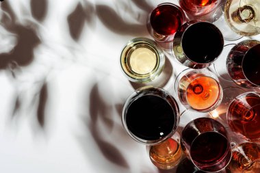 Beyaz arka planda kırmızı, gül ve beyaz şarap bardakları, üst manzara. Şarap barı, dükkan, şaraphane, şarap tatma konsepti. Sert ışık ve sert gölgeler