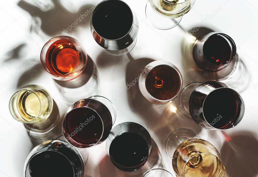 Red, rose and white wine in glasses on white background, top view. Wine bar, shop, winery, wine tasting concept. Hard light and harsh shadows