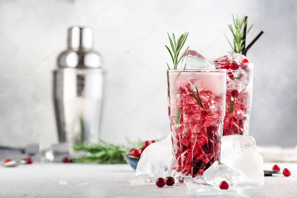 Cranberry cocktail with vodka, ice, juice, rosemary and red berries in highball glass. Refreshing long drink. Gray table background with negative space