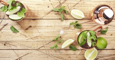 Limon, buz, zencefil birası, votka ve naneli bakır bardakta Moskova katırı kokteyli. Ahşap arkaplan, çubuk araçları, negatif boşluk, üst görünüm