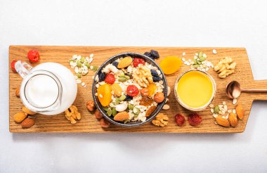 Müsli kasesi ve sağlıklı kahvaltı malzemeleri. Granola, fındık, kurutulmuş meyve, gevrek, bal ve Yunan yoğurdu beyaz masa üzerinde fotokopi alanı 