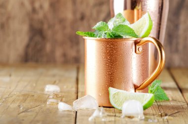 Limon, buz, zencefil birası, votka ve naneli bakır bardakta Moskova katırı kokteyli. Ahşap arkaplan, çubuk araçları, negatif boşluk