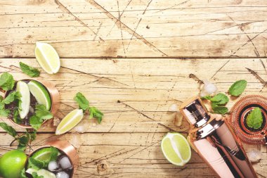 Limon, buz, zencefil birası, votka ve naneli bakır bardakta Moskova katırı kokteyli. Ahşap arkaplan, çubuk araçları, negatif boşluk, üst görünüm