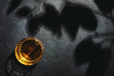 Amerikan viskisi bardakta ve şişede, siyah arka plan gölge desenli ve negatif alan